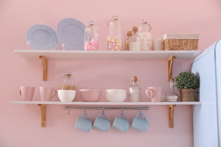 Shelves with dishware and products on pink wall in kitchenの写真素材
