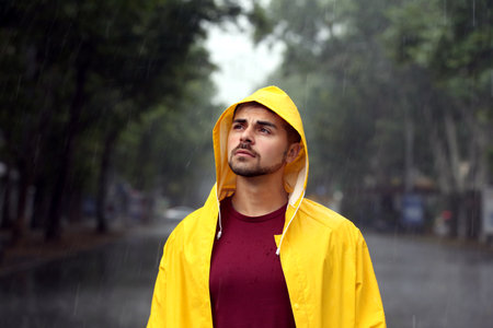 Thoughtful young man in bright coat outdoors on rainy dayの写真素材