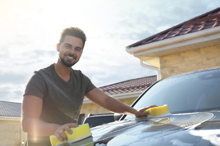 Young happy man washing car at backyard on sunny dayの写真素材
