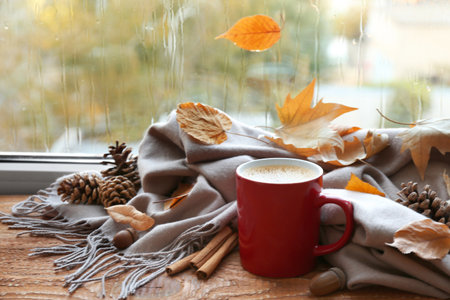 Cup of hot drink, scarf and autumn leaves on windowsill. Cozy atmosphereの写真素材