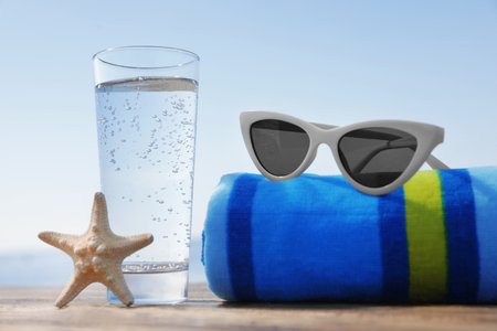 Wooden deck with glass of refreshing drink and beach accessories on hot summer dayの写真素材