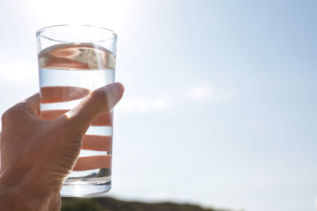 Woman holding glass of refreshing drink against blue sky on hot summer day, closeup. Space for text