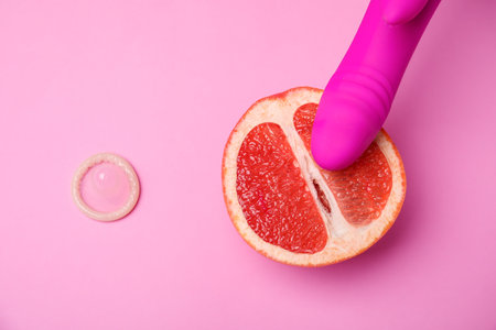 Half of grapefruit, purple vibrator and condom on pink background, flat lay. sex conceptの写真素材