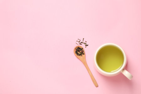 Spoon with green tea leaves and cup of hot beverage on pink background, flat lay. Space for textの写真素材