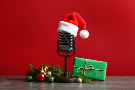 Microphone with Santa hat and decorations on gray table against red background. christmas musicの写真素材