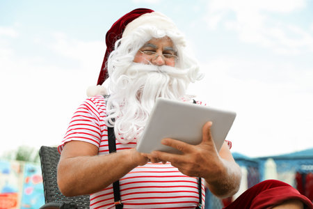 Authentic Santa Claus with tablet working on lounge chair at resortの写真素材