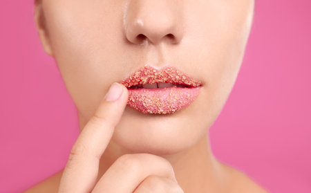 Young woman with sugar scrub on lips against pink background, closeupの写真素材