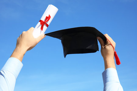 Student with graduation hat and diploma against blue sky, closeupの写真素材