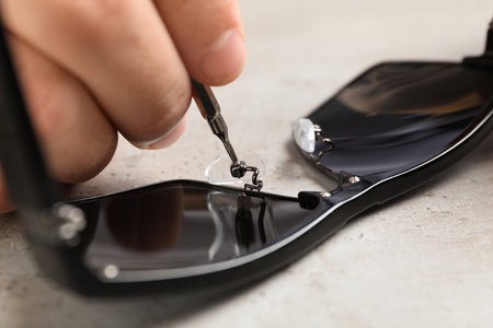 Handyman repairing sunglasses with screwdriver at gray table, closeupの写真素材