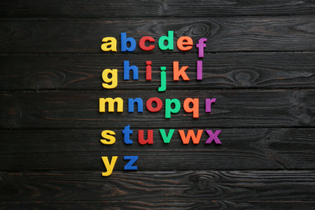 Colorful magnetic letters on black wooden background, flat lay. alphabetical orderの写真素材