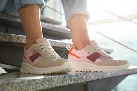 Young woman in stylish sneakers sitting on gray stairs indoors, closeup