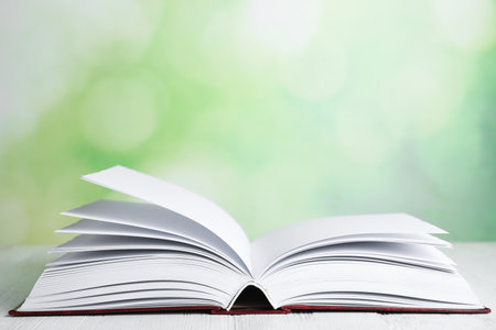 Open book on white wooden table against blurred green background. Space for textの写真素材