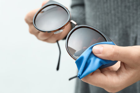 Woman wiping sunglasses with microfiber cleaning cloth on light background, closeupの写真素材