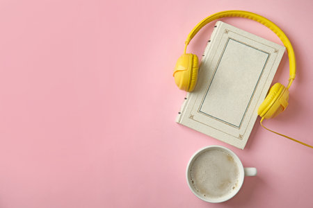 Modern headphones with hardcover book and coffee on pink background, top view. Space for textの写真素材