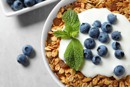 Delicious yogurt with granola and blueberries in bowl on gray table, top view