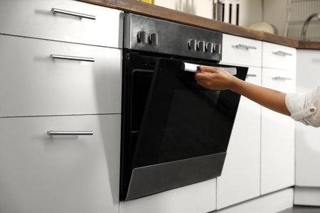 Woman opening modern electric oven in kitchen, closeupの写真素材