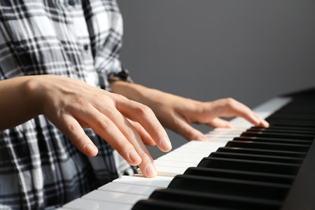 Young woman playing piano against gray background, closeupの写真素材