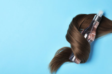 Spray bottle wrapped in lock of hair on light blue background, flat lay with space for text. natural cosmetic productsの写真素材
