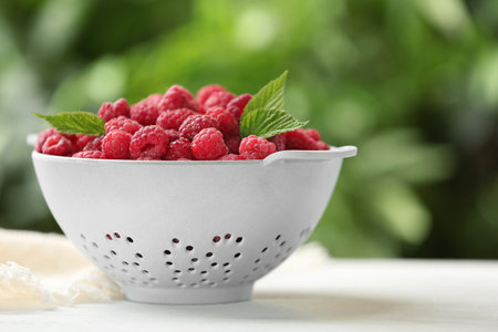 Colander with delicious ripe raspberries on white table against blurred background, space for textの写真素材