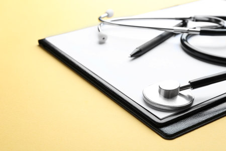 Clipboard with stethoscope and pen on yellow background, closeup. Space for textの写真素材