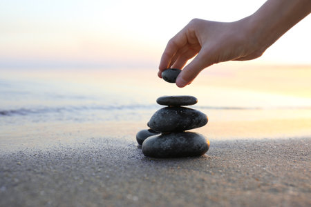 Woman stacking dark stones on sand near sea, space for text. Zen conceptの写真素材