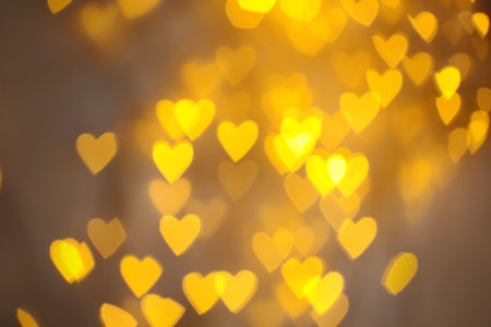 Blurred view of gold heart shaped lights on light backgroundの写真素材