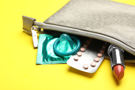 Cosmetic bag with contraceptives and red lipstick on yellow background, closeup. safe sex conceptの写真素材