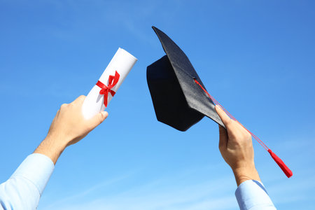 Student with graduation hat and diploma against blue sky, closeupの写真素材