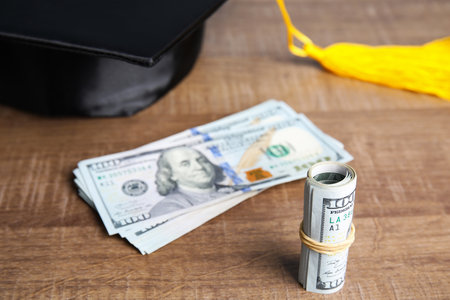 Dollar banknotes and student graduation hat on wooden background. Tuition fees conceptの写真素材