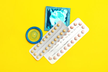 Condoms and birth control pills on yellow background, flat lay. safe sex conceptの写真素材