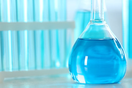 Volumetric flask with light blue liquid on table, closeup. Space for textの写真素材