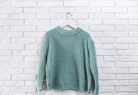 Hanger with stylish sweater on brick wall