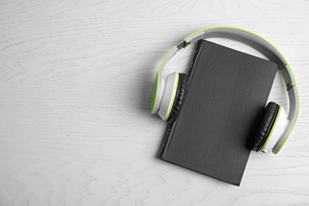 Modern headphones with hardcover book on white wooden background, top view. Space for text