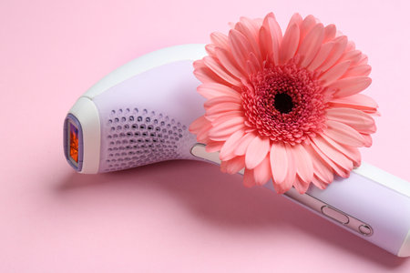 Modern photoepilator and flower on pink background, closeup