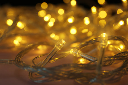 Glowing Christmas lights on color background, closeup view