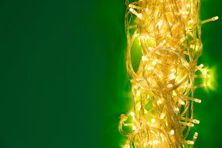 Glowing Christmas lights on green background, top view. Space for textの写真素材