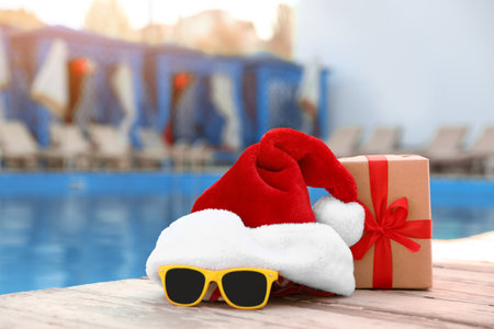 Authentic Santa Claus hat, gift box and sunglasses near pool at resortの写真素材