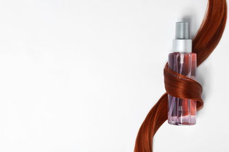 Spray bottle wrapped in lock of hair on white background, top view. natural cosmetic productsの写真素材