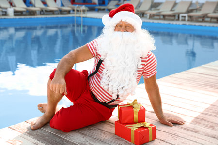 Authentic Santa Claus with gift boxes near pool at resortの写真素材