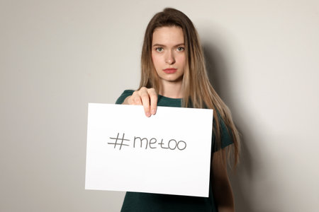Young woman holding #METOO card against light backgroundの写真素材