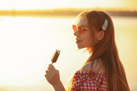 Beautiful young woman with ice cream outdoors at sunsetの写真素材