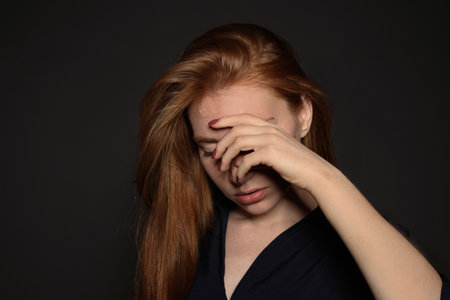 young woman covering face against dark backgroundの写真素材