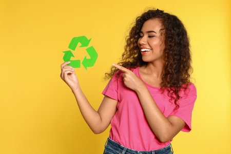 Young African-American woman with recycling symbol on yellow backgroundの写真素材