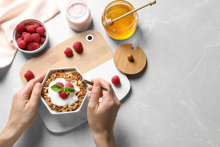Woman eating delicious yogurt with granola and raspberries at gray table, top view. Space for textの写真素材
