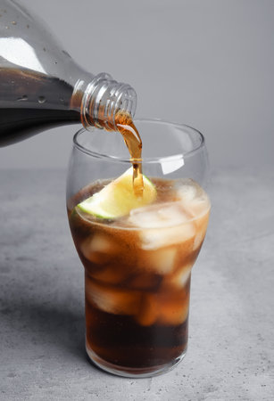 Pouring refreshing soda drink into glass on table against gray background