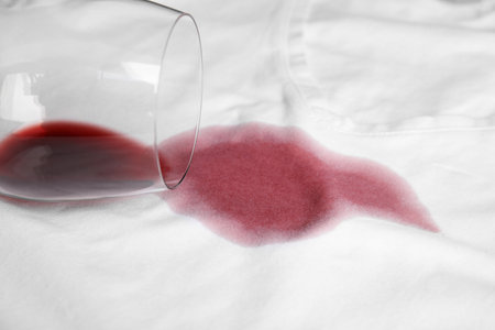 Overturned glass and spilled exquisite red wine on white t-shirt. Space for textの写真素材