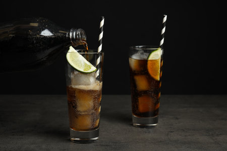 Pouring refreshing soda drink into glass on gray table against black backgroundの写真素材