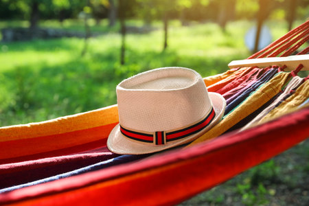 Bright comfortable hammock with hat hanging in green garden, closeupの写真素材