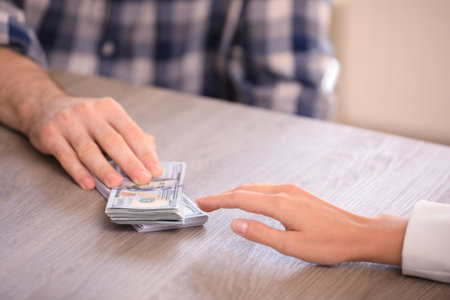 Man giving dollar bills to businesswoman at wooden table, closeup