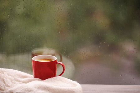 Cup of drink and blanket on windowsill, space for text. rainy weatherの写真素材